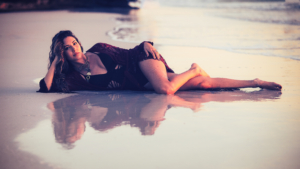 Young woman lays in the water line at sunset